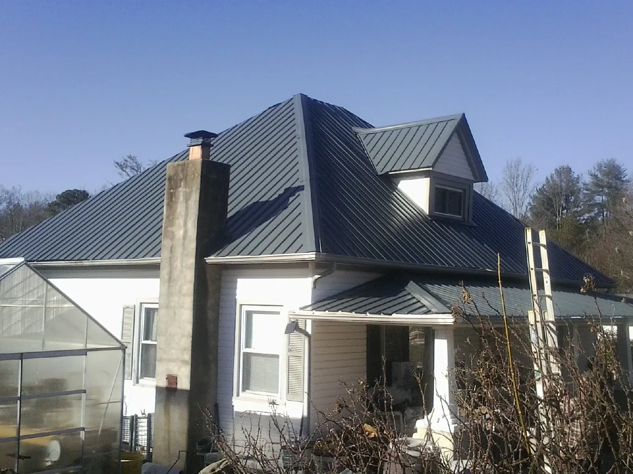 Dark blue standing seam metal roof on a white farmhouse with dormer — Slate & Tile Roof Repair by Roofing Brothers in Mc Dade