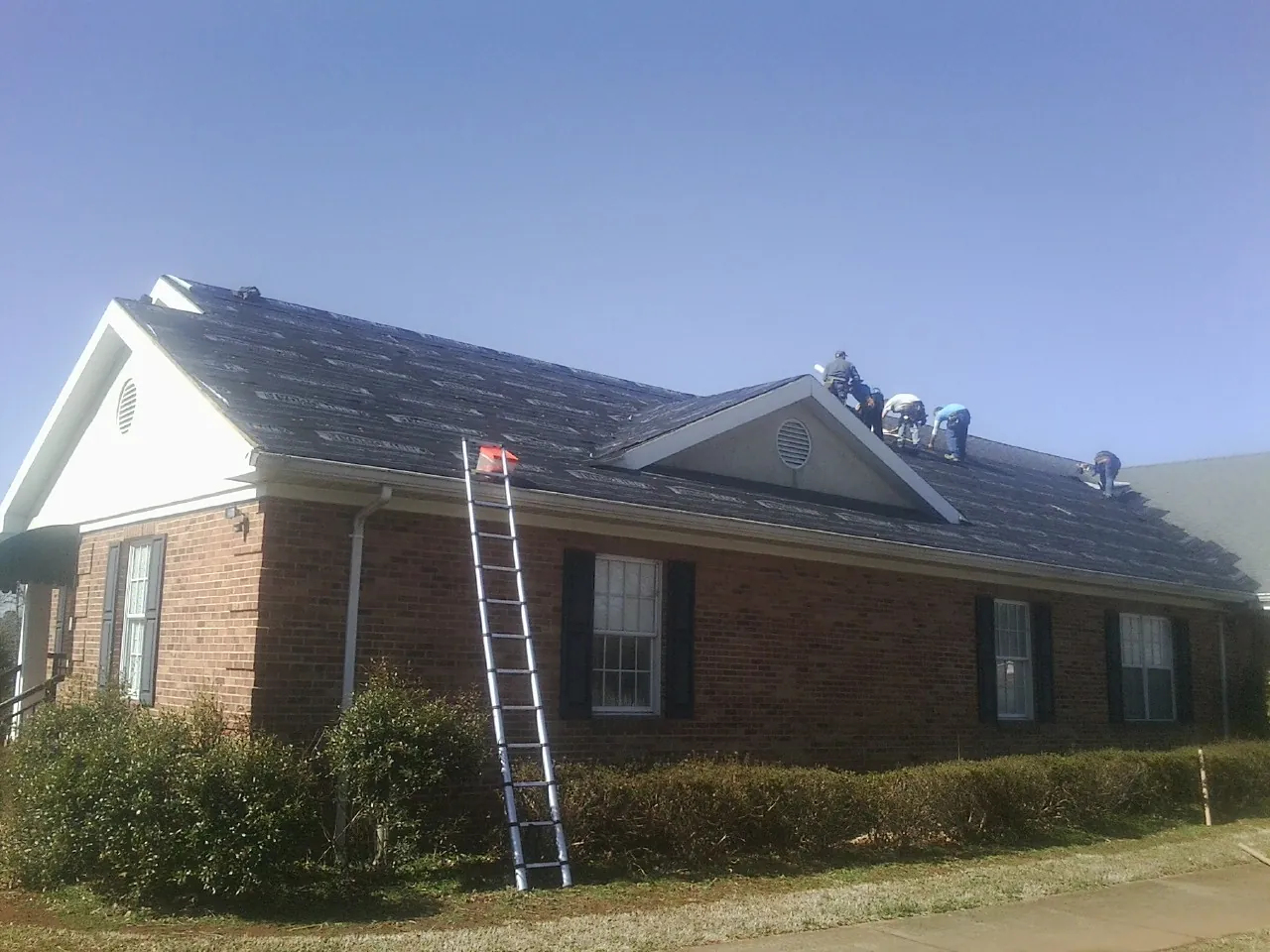 Crew tearing shingles off a brick ranch roof with a ladder set — Metal Roof Repair work by our crew in Mc Dade