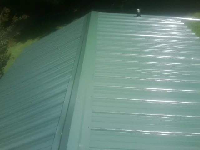 New green metal panels meeting at the ridge of a roof — Flat Roof Repair work by our crew in Mc Dade