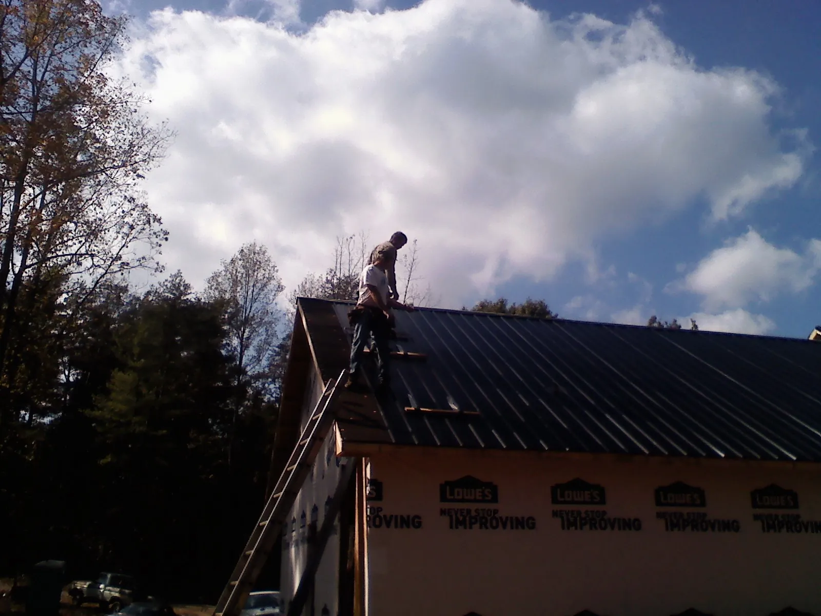 Roofer fastening dark metal panels high against a cloudy sky, from a Roof Inspection job in Mc Dade