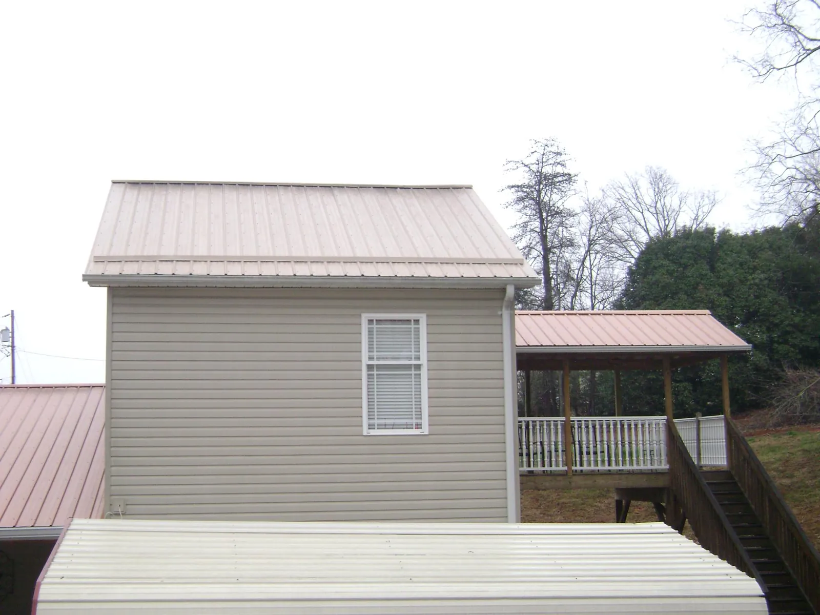 Tan metal roofs on a two story addition and attached porch, from a Roof Replacement job in Mc Dade